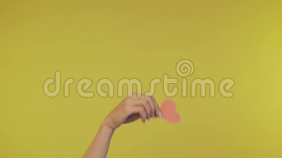 女性的手整齐地在一个孤立的黄色背景上握住一个小纸心4K视频的预览图