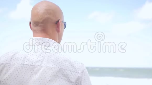 站在海滩上的秃头的后景他在看海近距离射击视频的预览图