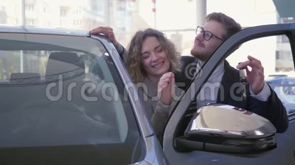 快乐购车者年轻情侣们喜欢新车的肖像并在汽车沙龙中展示钥匙视频的预览图