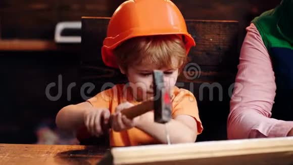 戴着头盔的孩子可爱地扮演建筑工人或修理工修理或手工制作小孩把钉子钉在木板上视频的预览图
