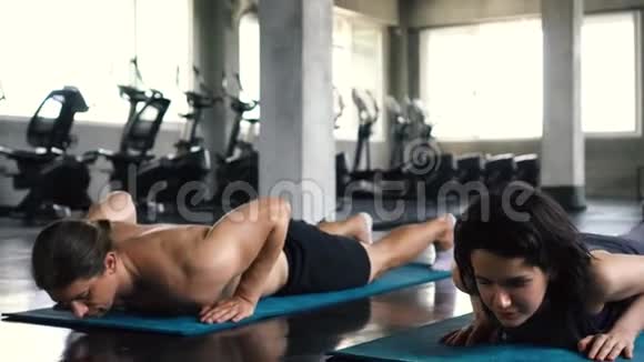 年轻的女人和男人在健身房地板上用向上的狗和向下的狗姿势练习瑜伽两个夫妇在工作视频的预览图