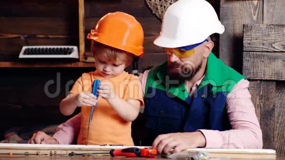 男孩忙于保护头盔学习用螺丝刀与爸爸拧螺丝车间和杂工概念爸爸和爸爸视频的预览图