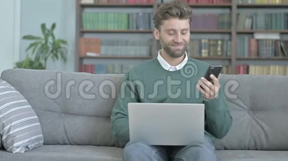 年轻人一边打电话一边微笑一边手提电脑视频的预览图
