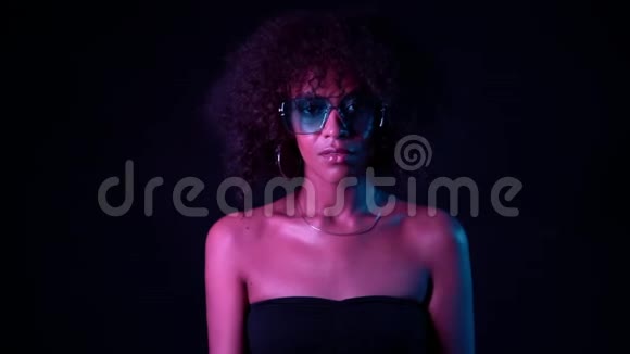 年轻性感的非洲女孩的肖像蓝色眼镜粉红色霓虹灯在黑色背景完美妆容的女人视频的预览图
