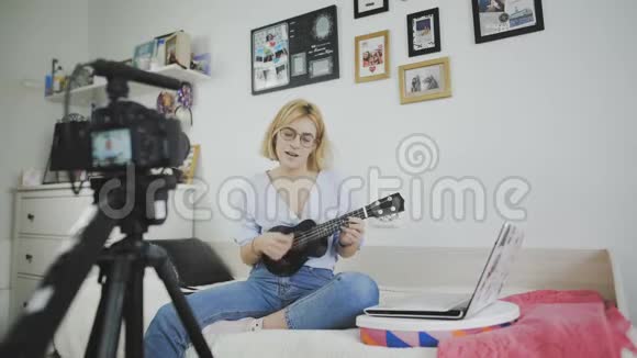 年轻迷人的女孩时尚博主正在用相机录制视频唱歌和弹吉他视频的预览图