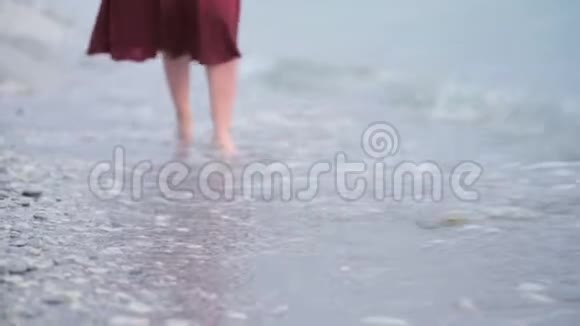 一个穿着红色衣服的年轻女孩的特写腿在潮湿的海岸上翻滚着波浪把焦点转移到焦点上视频的预览图