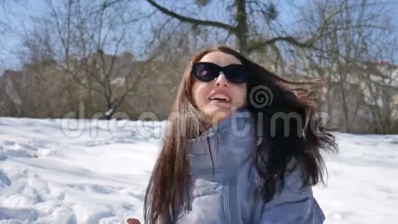 早上穿着黑色太阳镜和黑色直发的年轻女孩在公园户外玩雪球视频的预览图