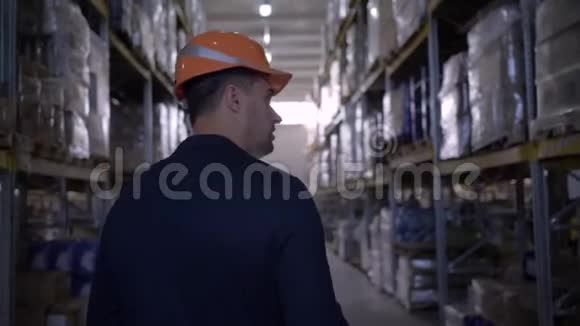 穿着安全帽和西装穿过仓库的商人在平板电脑上做笔记视频的预览图