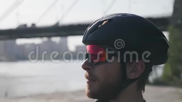年轻的白种人留着大胡子的骑自行车的人看起来很直骑自行车的人戴着黑色头盔和太阳镜的肖像慢动作视频的预览图