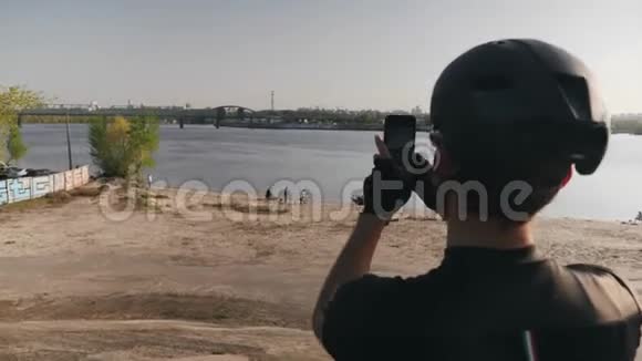 骑自行车的人拿着相机拍着河和城市站在山上的照片桥和太阳在背景中闪耀视频的预览图
