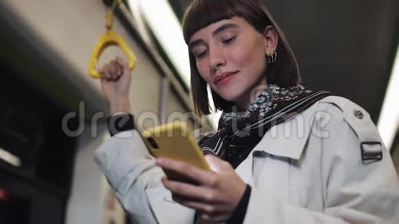 公共交通中微笑的美丽年轻女子的肖像抓住扶手在黄色智能手机上浏览城市视频的预览图