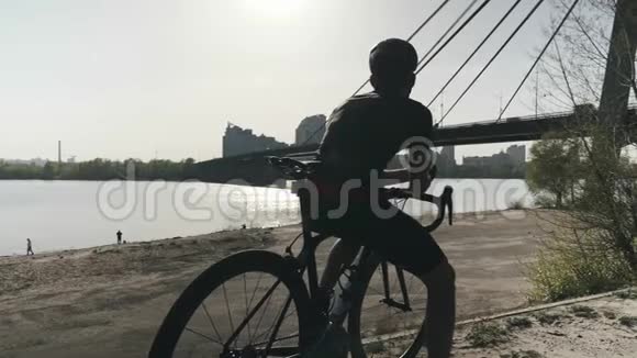 强壮健康的运动骑自行车的人坐在自行车上前方梦想着未来桥和河的背景慢慢视频的预览图