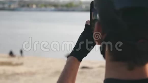 年轻的骑自行车的人手里拿着电话戴着头盔太阳镜和手套在河和城市拍照视频的预览图