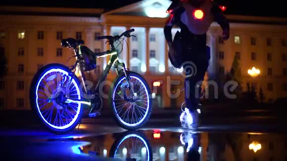 发光的自行车倒映在水中一个穿着发光鞋的男人围着一辆未来派自行车跳舞视频的预览图