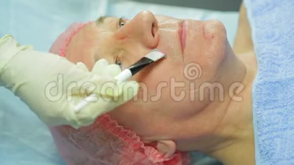戴手套的女美容师用一个带刷子的治疗粘土面具对着男人的脸视频的预览图