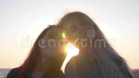 几个年轻的女人头对头享受日落风吹毛求疵沙滩阳光透过头发使头发视频的预览图