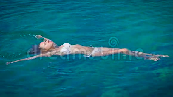 穿着白色比基尼在蔚蓝的大海中游泳的年轻快乐女人视频的预览图
