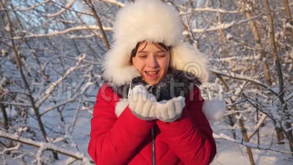 小女孩从她的手中吹起雪花在冬天的公园里被夕阳照亮快乐的女孩在日落时吹雪花视频的预览图