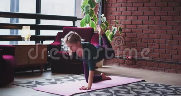 金发的运动型女士做瑜伽运动在家里伸展身体在垫子上美丽而现代的内部和大的内部视频的预览图