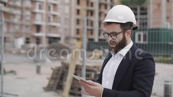年轻的胡子建筑师在工地用平板电脑拍照他穿着商务服视频的预览图