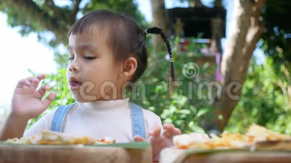 可爱的饥饿的女孩喜欢在后院吃自制的披萨有家人的小女孩在户外的午餐桌上选择性泡沫视频的预览图
