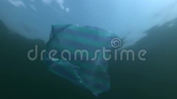 塑料污染用条纹袋在水面下游泳在太阳光线下在背景蓝天上与云低角度拍摄视频的预览图