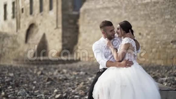美丽的童话新婚夫妇坐在一起拥抱在高高的砖墙上分享爱行动视频的预览图