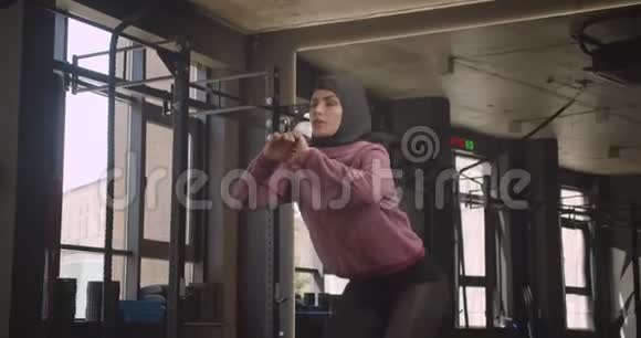 年轻有魅力的穆斯林女性在室内健身房蹲着的特写照片视频的预览图