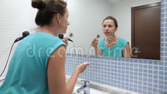 漂亮的女人在浴室镜子前用化妆刷粉脸视频的预览图