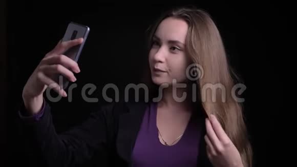年轻有魅力的白种人长发女性在电话中自拍并在面前摆姿势的特写镜头视频的预览图