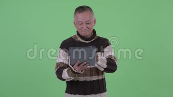 快乐成熟的日本男人一边思考一边用数码平板电脑说话视频的预览图
