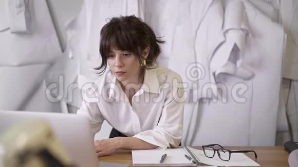 女设计师在缝纫室的桌子上拿着笔记本电脑视频的预览图