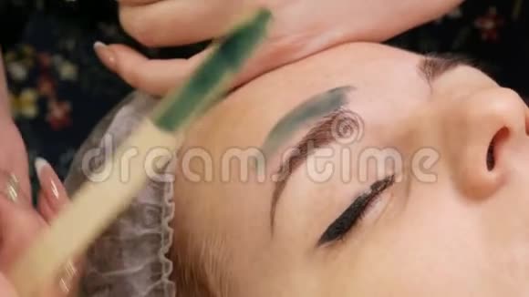 眉毛形状的蜡校正美容师在眉毛上涂上温暖的绿色蜡去除多余的头发视频的预览图