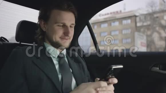 一个英俊的男人棕色头发穿着开心果衬衫穿着灰色西装坐在车里通过手机输入信息视频的预览图