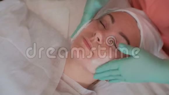 戴着绿色手套的美容师给一个漂亮女孩的脸涂上肥皂美容女性皮肤清洁化妆品视频的预览图