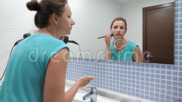 漂亮的女人在浴室镜子前用化妆刷粉脸视频的预览图