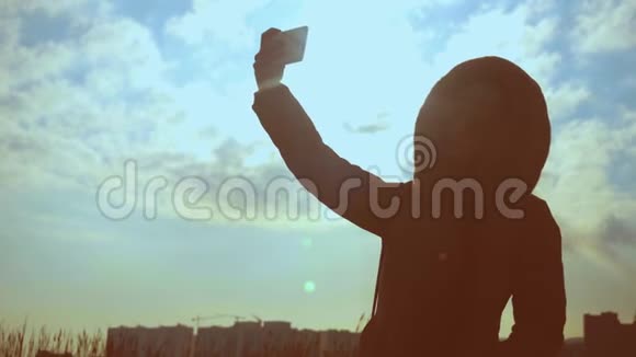 一位戴着自然眼镜的年轻女人的剪影在日落和建筑物的背景下自拍视频的预览图