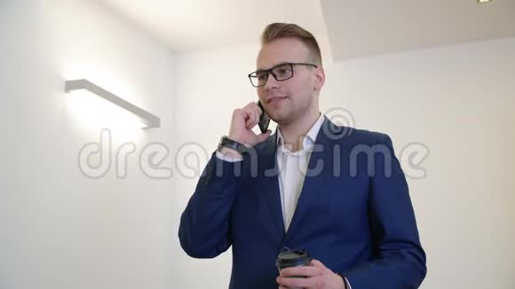 英俊的商人用手机说话办公室里拿着咖啡杯视频的预览图