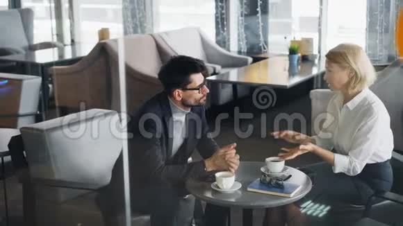 企业家们成熟的男人和女人坐在咖啡馆的桌子上交谈视频的预览图