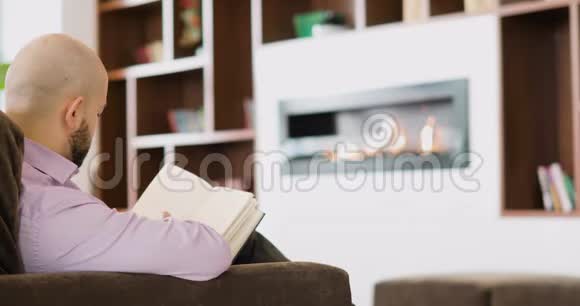 男人坐在壁炉前的沙发上在办公室里读一本书视频的预览图