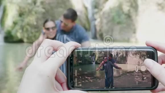 一对夫妇在瀑布附近用手机拍照视频的预览图