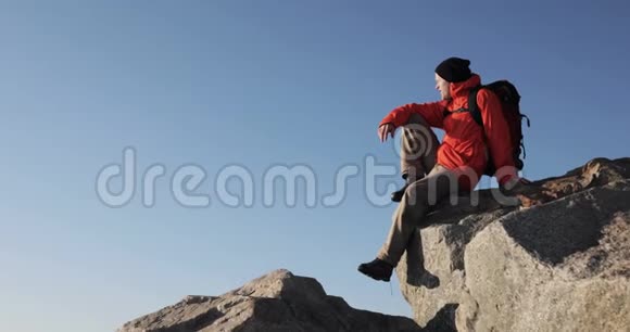 年轻人徒步旅行者正坐在悬崖的山顶上环顾四周手指向前侧视视频的预览图