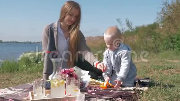 快乐的童年温暖的周末小妈妈和可爱的小男孩在河边的大自然野餐时玩玩具视频的预览图
