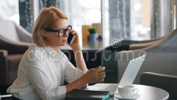 成熟的商务女士在咖啡馆里打手机和使用笔记本电脑视频的预览图
