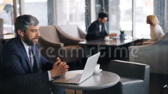 现代商人用无线耳机和笔记本电脑在咖啡馆里交流视频的预览图