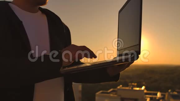 日落时分一名男性自由职业程序员坐在摩天大楼屋顶上手提电脑和键盘上的啤酒输入代码视频的预览图