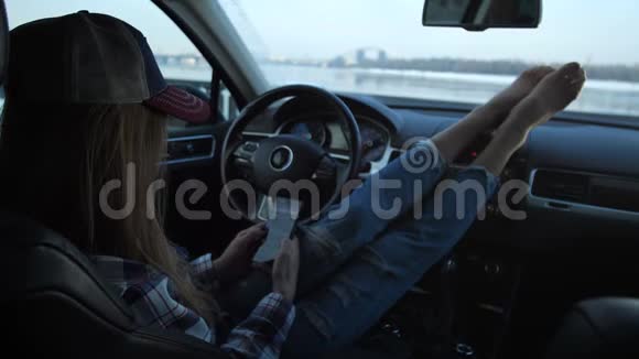 非常漂亮的视角一个时髦的女孩在车里看手机窗外你可以看到河视频的预览图