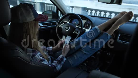 那个女孩坐在车里她的腿躺在面板上女孩看着手机为了冬天的公羊4K视频的预览图