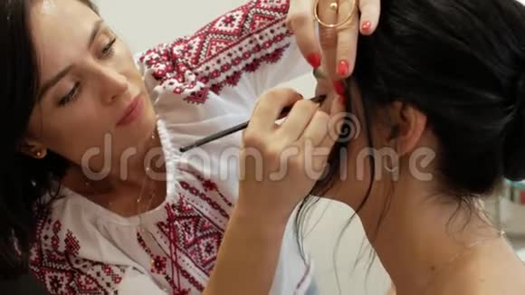 化妆师为一个漂亮的黑发女孩化妆设计师致力于模型的图像化妆师画眼睛视频的预览图