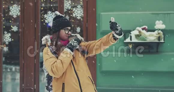 一个微笑的女孩在冬天的城市街道上下雪的背景下自拍视频的预览图